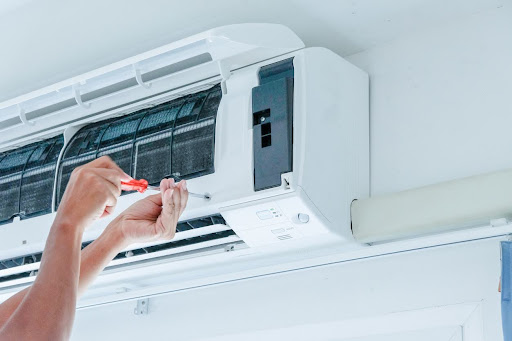 A technician is under an air conditioner unit using a screwdriver.